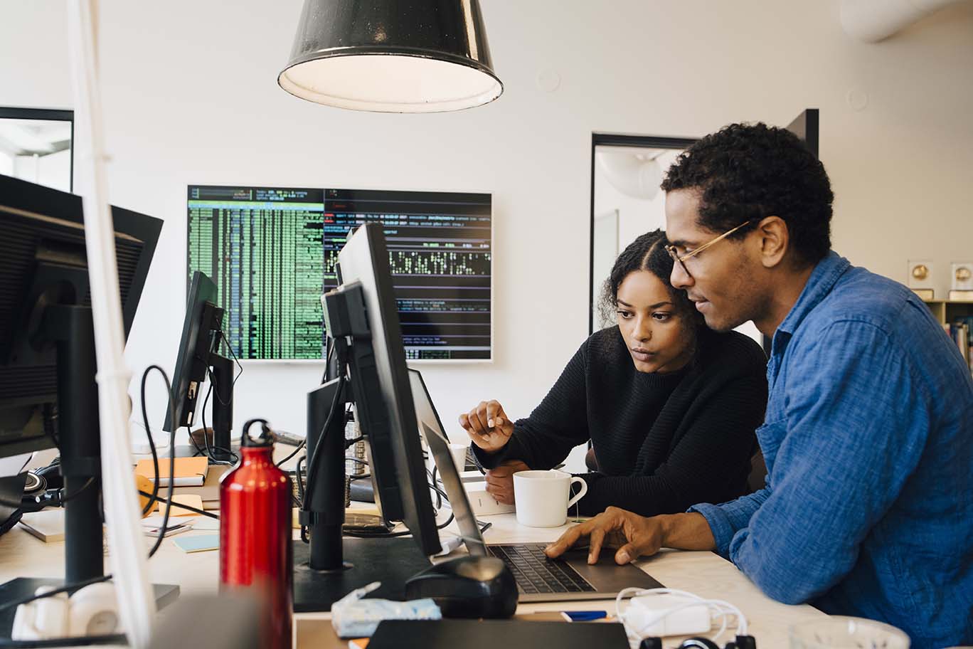  A male and female engineer in an office looking at a computer while coding.
